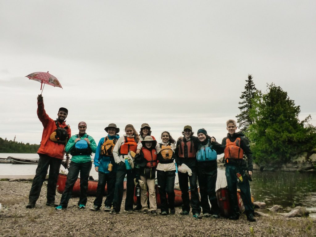 Group of people wearing life jackets and standing my canoes at the start of a trip