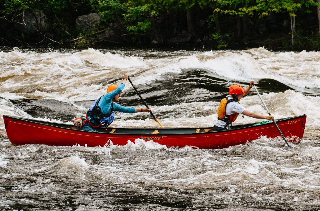 Two paddlers paddling in a red canoe upstream on the Madawaska River.
