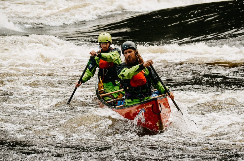 Two paddlers in green drysuits and red paddling life jackets on the Madawaska River.