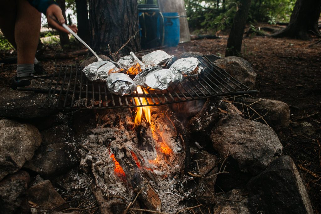 Breakfast sandwiches in tin foil on a fire at a campsite.