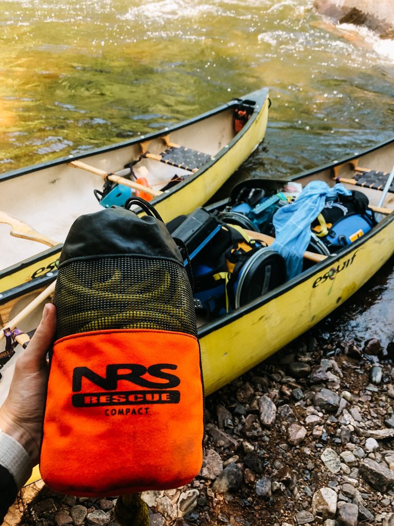 Рука держит сумку NRS над желтым каноэ на реке