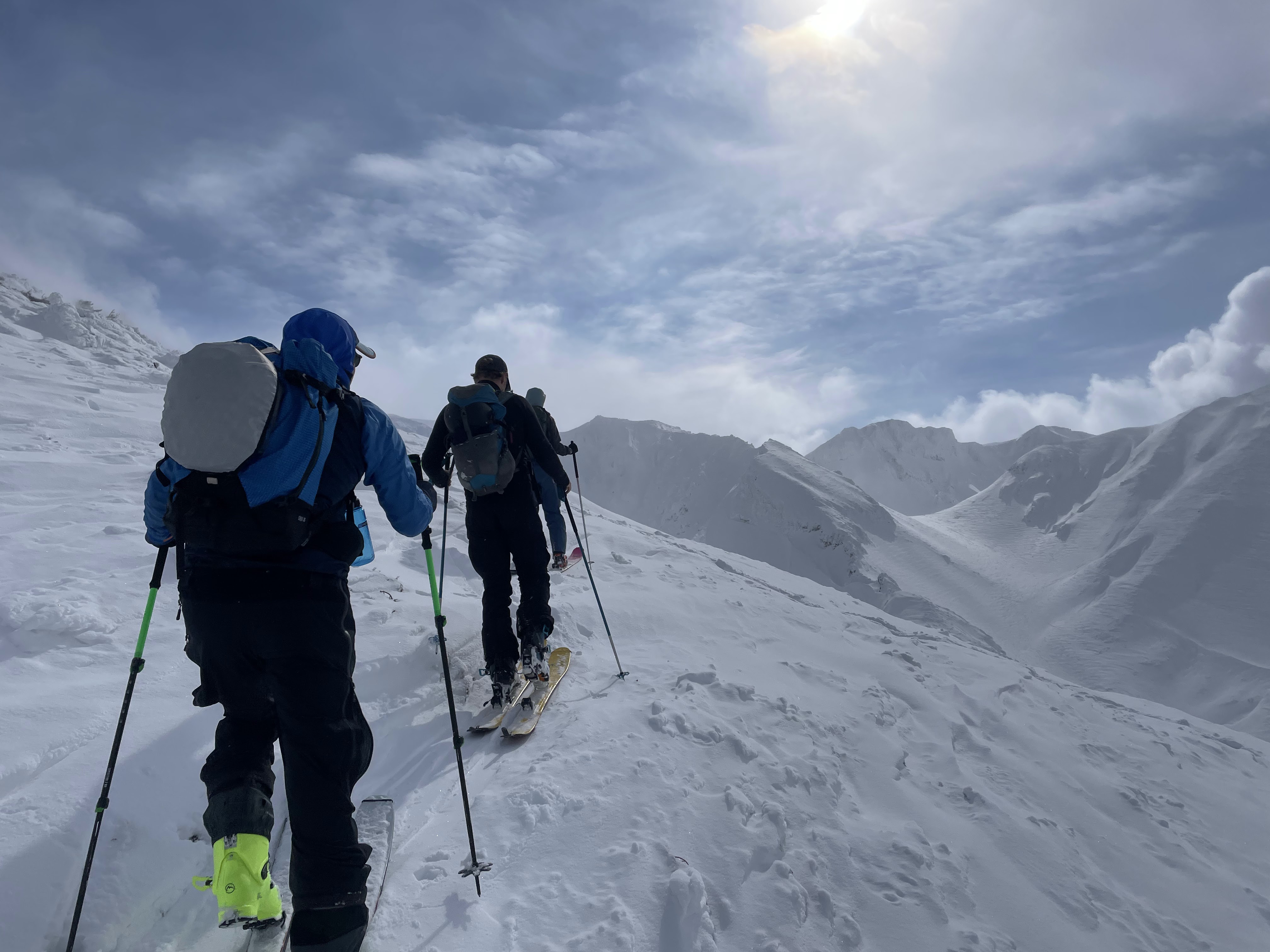 Трое лыжников движутся по гребню с высокими заснеженными горами рядом
